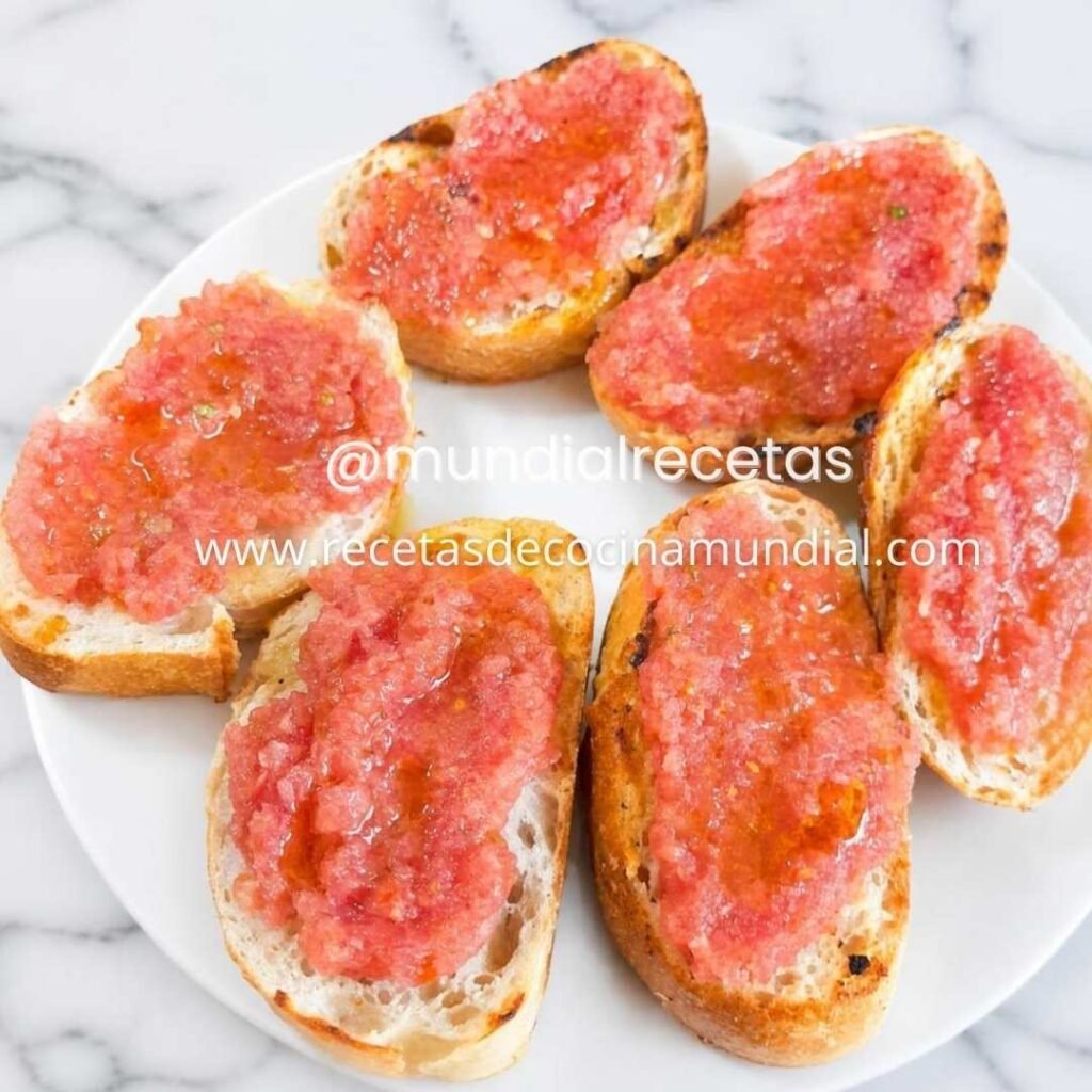Pan con tomate tradicional servido en un plato con pan rústico tostado, tomate fresco rallado y aceite de oliva virgen extra.